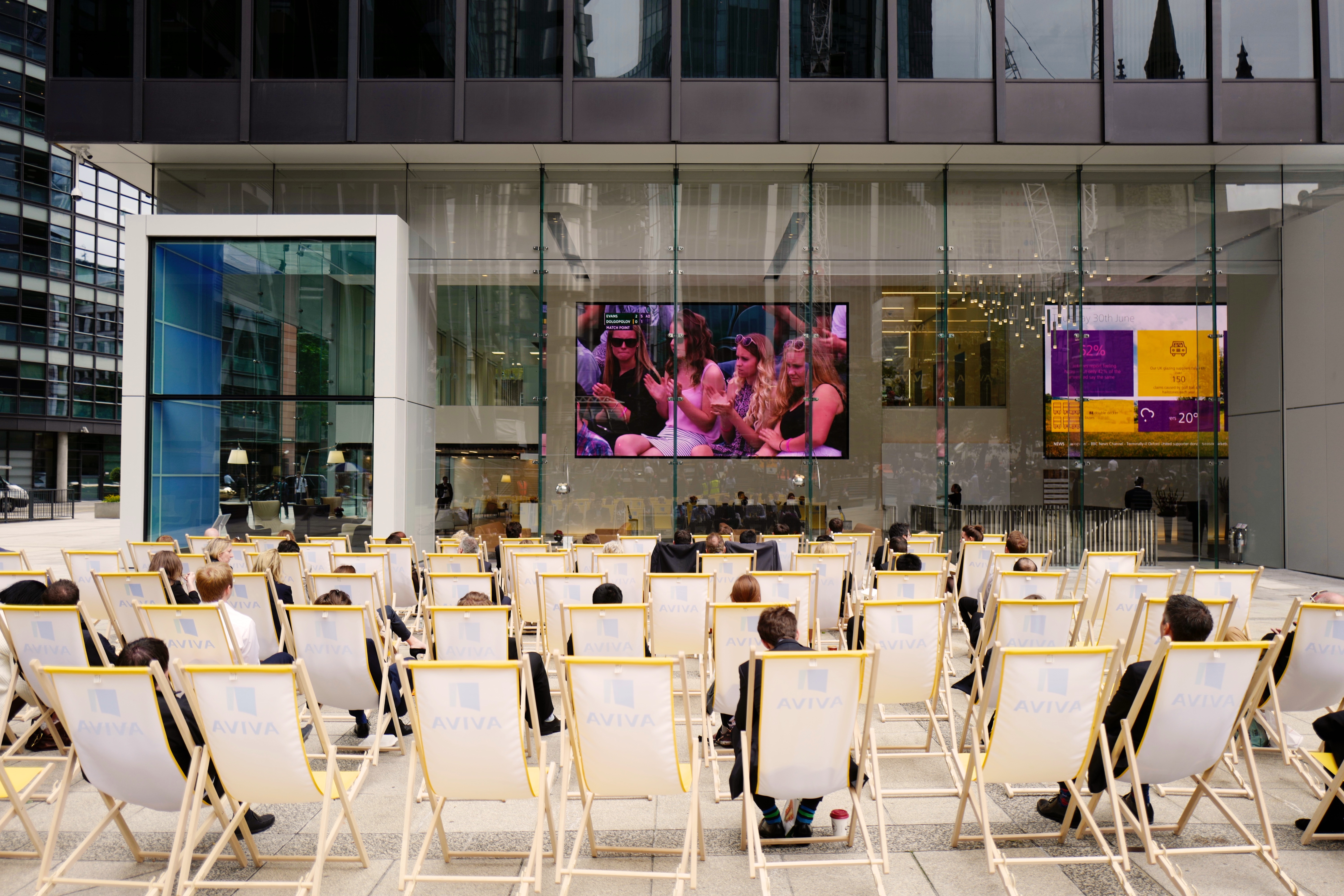 Lots of employees on Aviva branded deck chairs watching a large TV screen