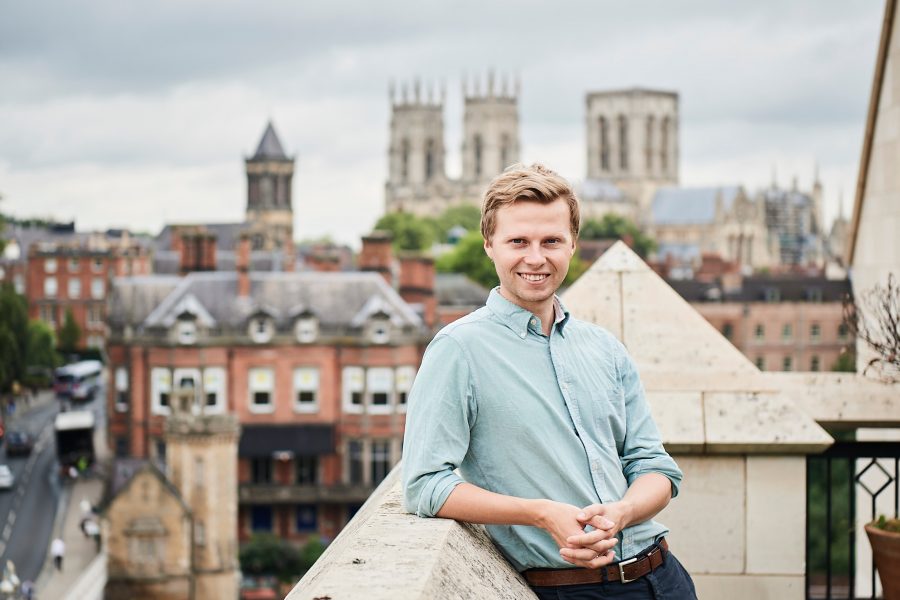 Man smiling at camera standing outside on the roof terrace at Wellington Row (Aviva York office) with the view of York Minster in the background
