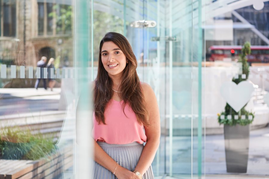 Woman stood by glass wall smiling at the camera