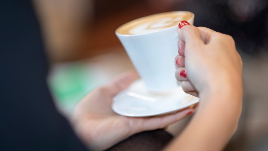 Close up of hands with red nails on a coffee cup and saucer